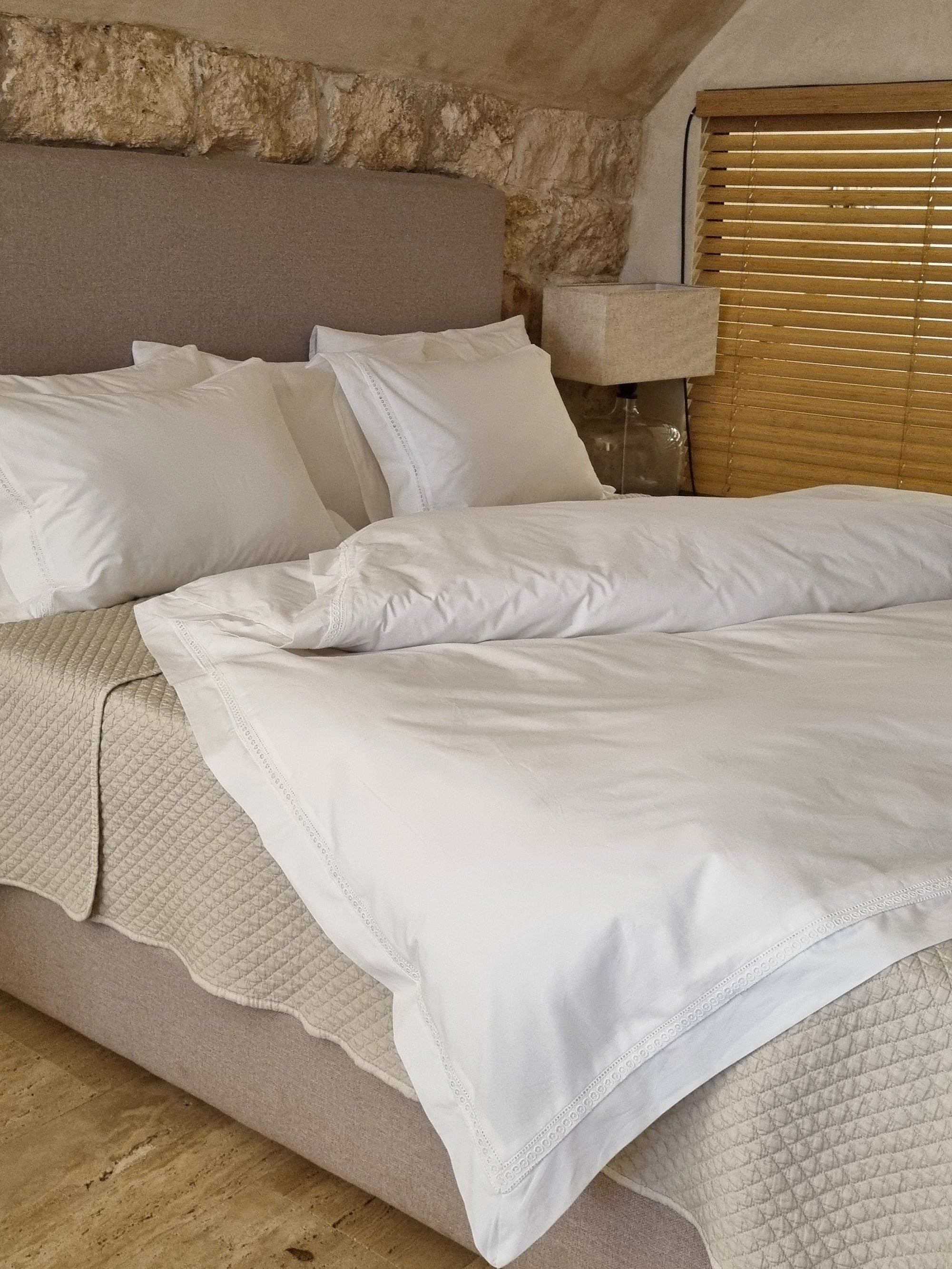 Bed with white bedding and pillows on a wooden floor.